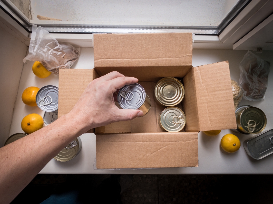 A person putting canned goods into a cardboard box