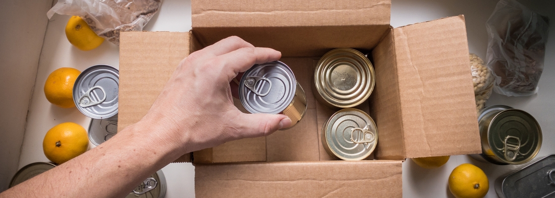 A person putting canned goods into a cardboard box